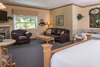 Bed facing a brown sofa with the jetted tub set beside a decorated stone mirror at Hilltop Inn, Salmon Arm