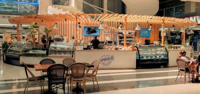 Express-O Coffee Shop\'s pastry counter with glass display cases set under a wooden pergola at Megapolis Outlets
