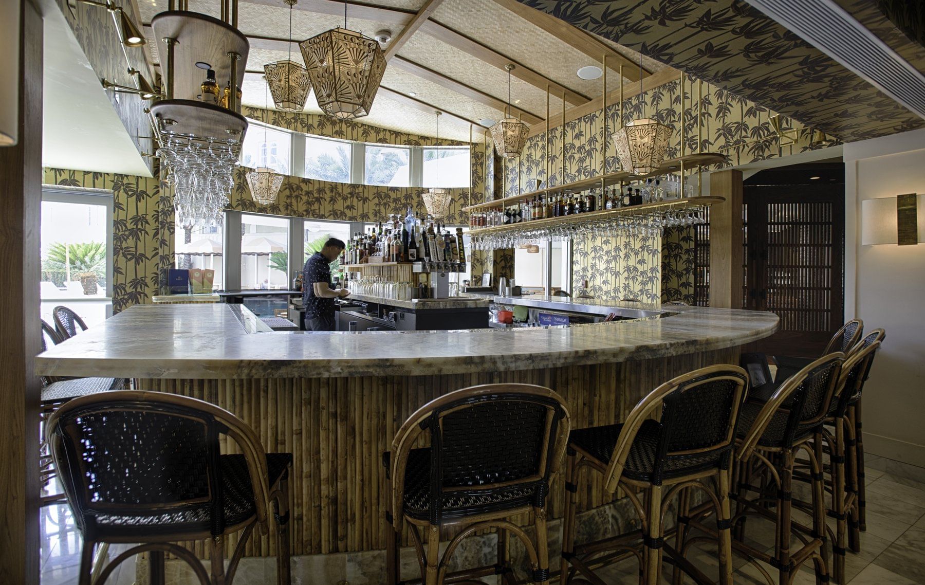 A bar with a marble countertop and stools, featuring a unique lighting fixture and wallpaper.