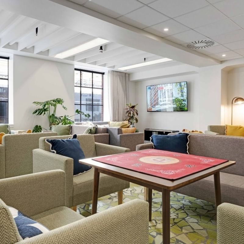 Bright communal lounge with comfortable seating, game table, plants, and large windows at UniLodge Auckland Central.