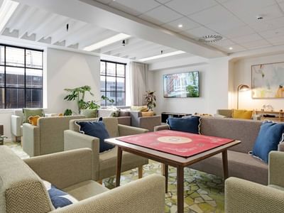 Bright communal lounge with comfortable seating, game table, plants, and large windows at UniLodge Auckland Central.