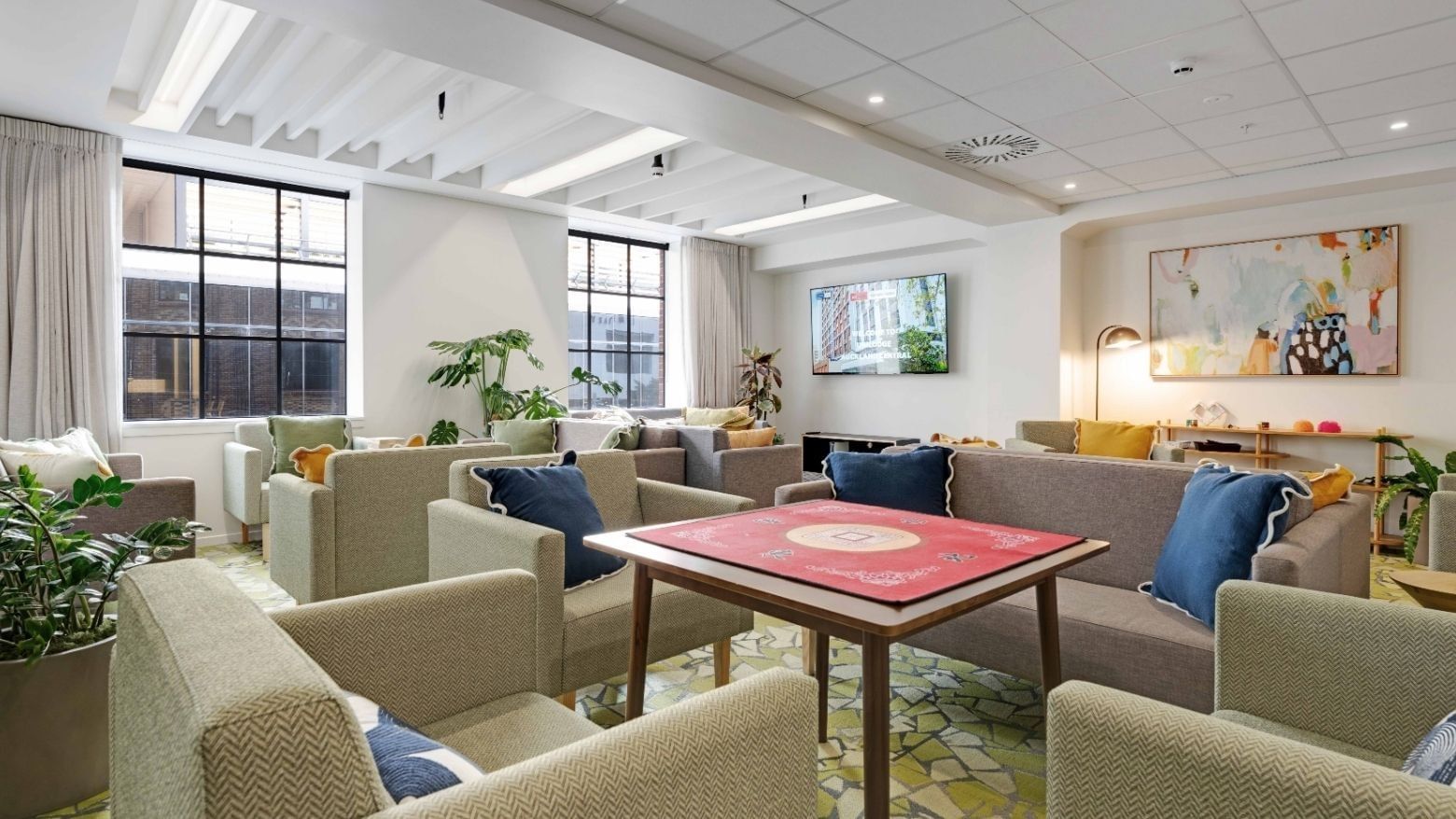 Bright communal lounge with comfortable seating, game table, plants, and large windows at UniLodge Auckland Central.