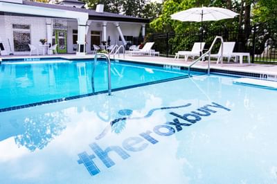 Outdoor pool with reflective surface surrounded by lounge chairs and a sunny patio area at The Roxbury