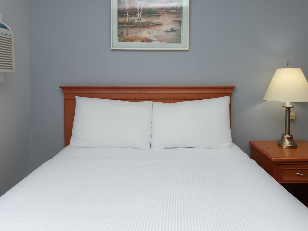 Queen bed with white linens, wooden headboard, nightstand, and framed artwork.