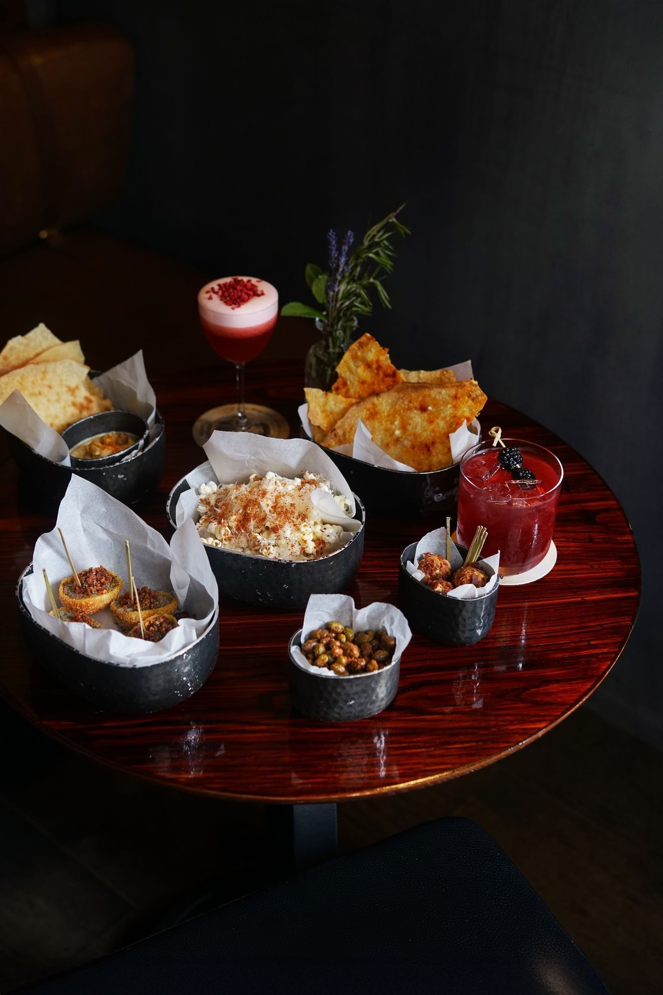 A variety of appetizers and cocktails arranged on a polished wooden table in Joshua's Tavern at The Londoner Hotel