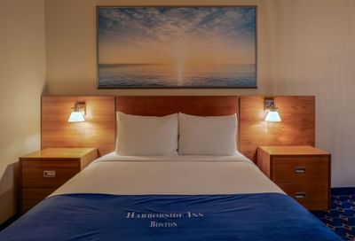 Bed between the sidetables and skyline art above the exposed brick wall in Queen City View at Harborside Inn Boston