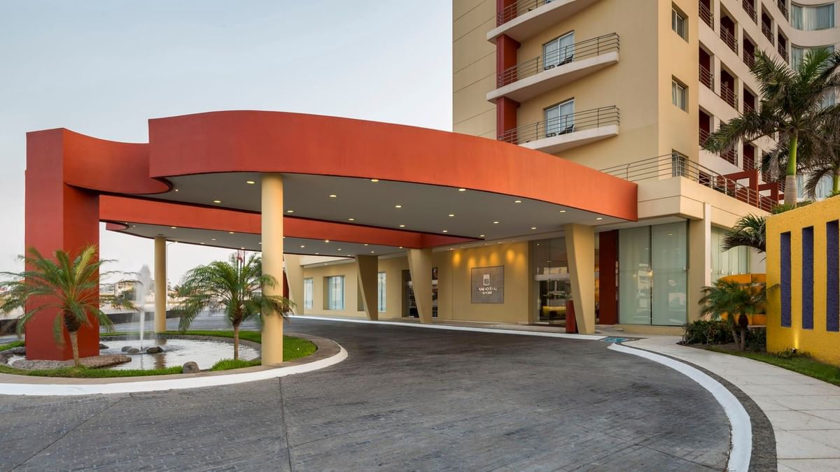Modern architectural entrance and driveway at Camino Real Veracruz, featuring a bold red canopy and palms
