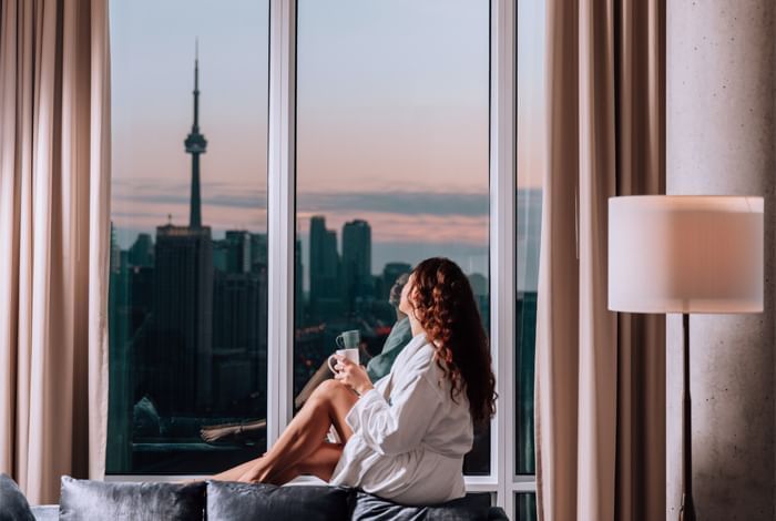 Femme se relaxant avec une tasse de café près de la fenêtre de l'hôtel X Toronto