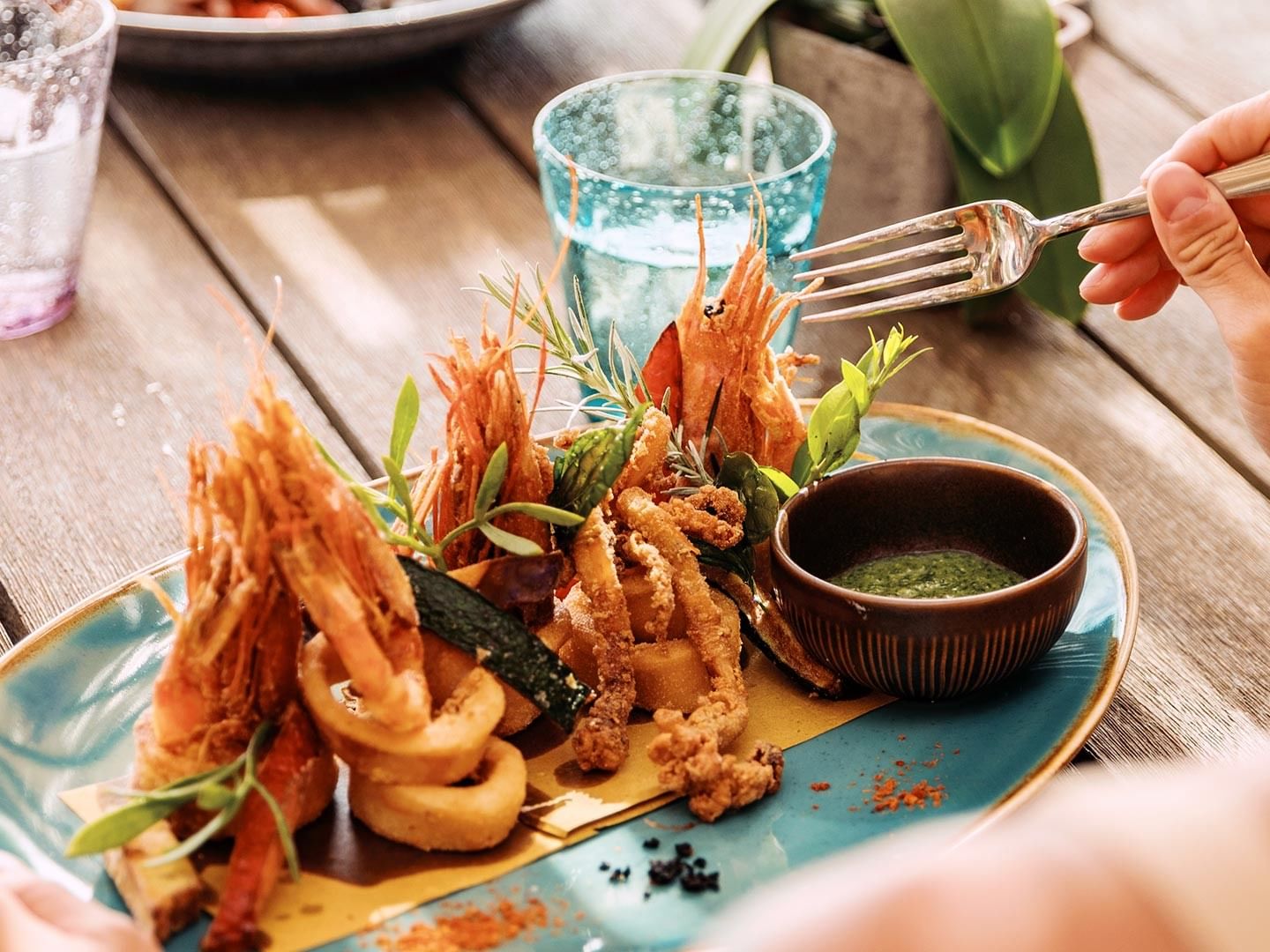 A person is eating a seafood dish with a fork on a blue plate.