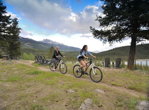 Two woman riding bikes on trails with mountains in background