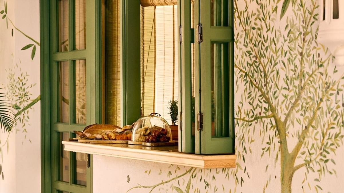 El Obrador features a charming service window with green shutters, wicker stools, and tropical plants at Marbella Club