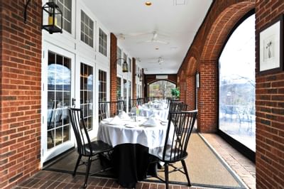 Evergreens restaurant dining space with white cloth tables and black chairs facing large windows at The Simsbury Inn