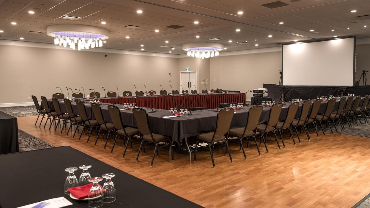Conference hall setup with long tables, chairs, and a projection screen at Coast Nisku Inn & Conference Centre.