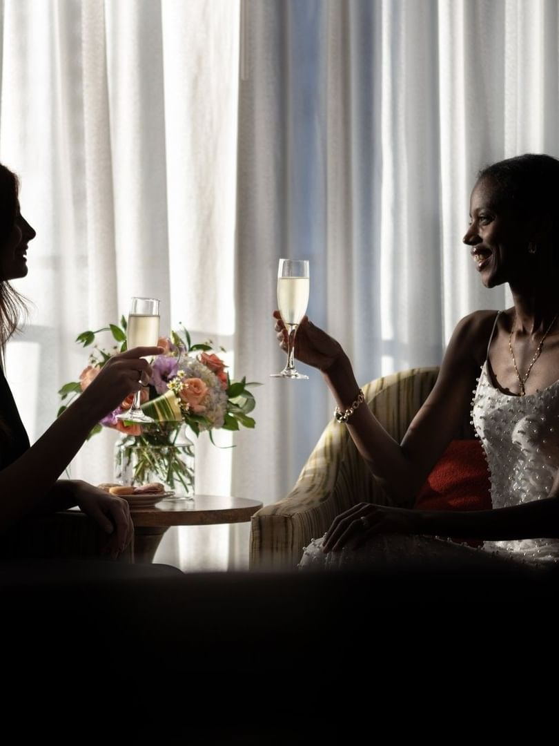 Silhouetted guests raising champagne flutes by a floral vase under soft light at Warwick Seattle
