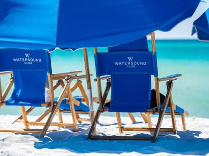 Two blue branded beach chairs with matching umbrella on white sand facing turquoise ocean waters