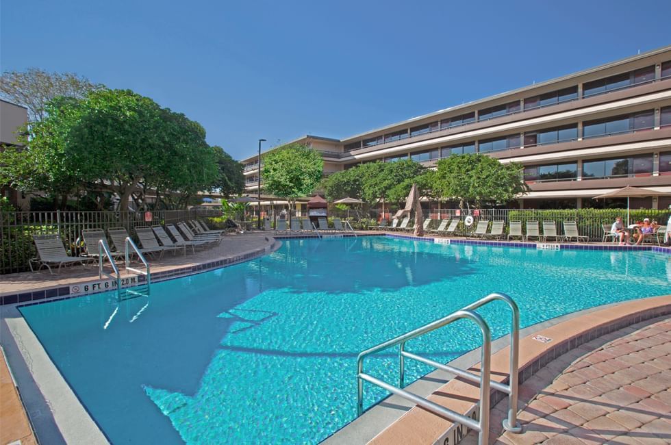 A large pool surrounded by lounge chairs and a long hotel building. 