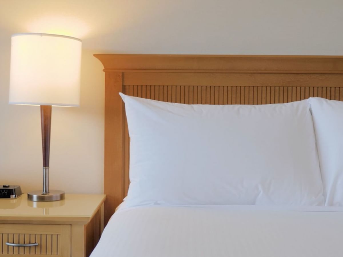 Bed with fitted white sheets, pillows and side lamp