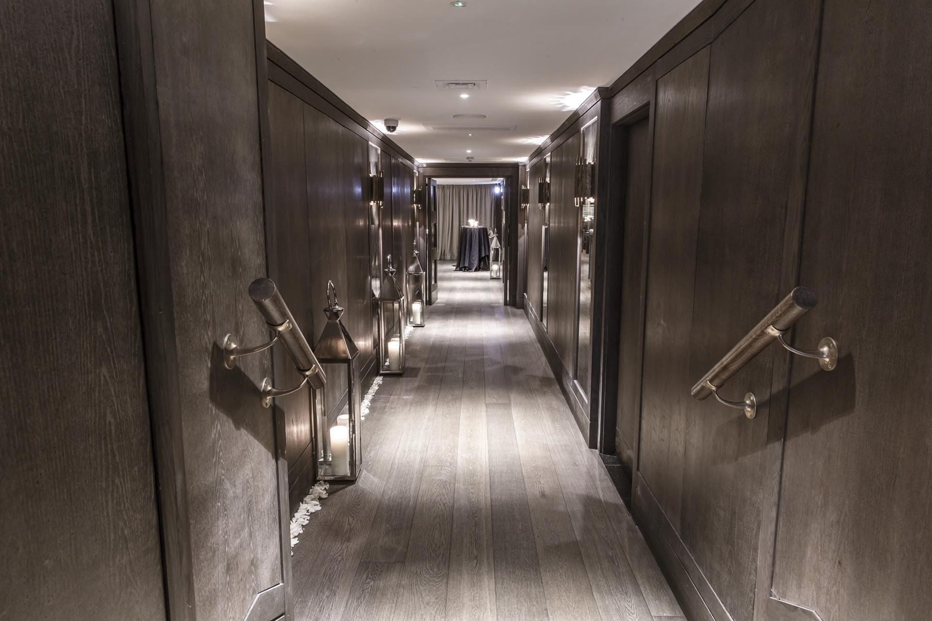Elegant hallway with dark wood paneling, lighted sconces, and a long wooden floor at The May Fair Hotel leading up to the Private Dining Room.