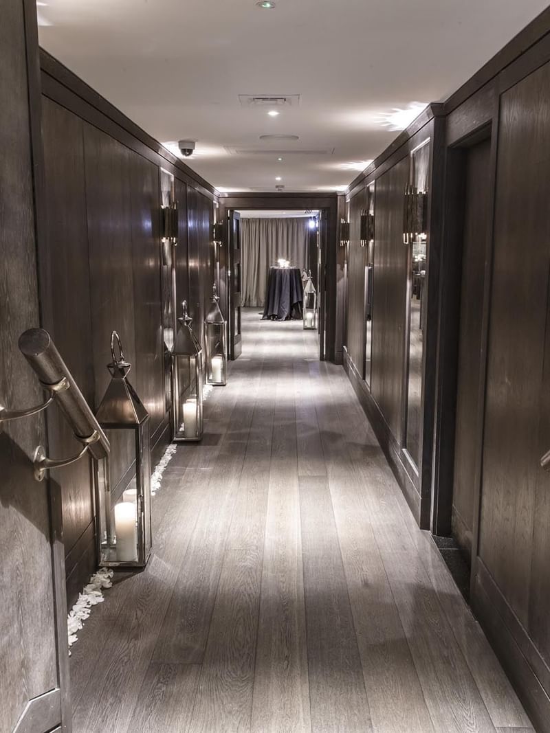 Elegant hallway with dark wood paneling, lighted sconces, and a long wooden floor at The May Fair Hotel leading up to the Private Dining Room.