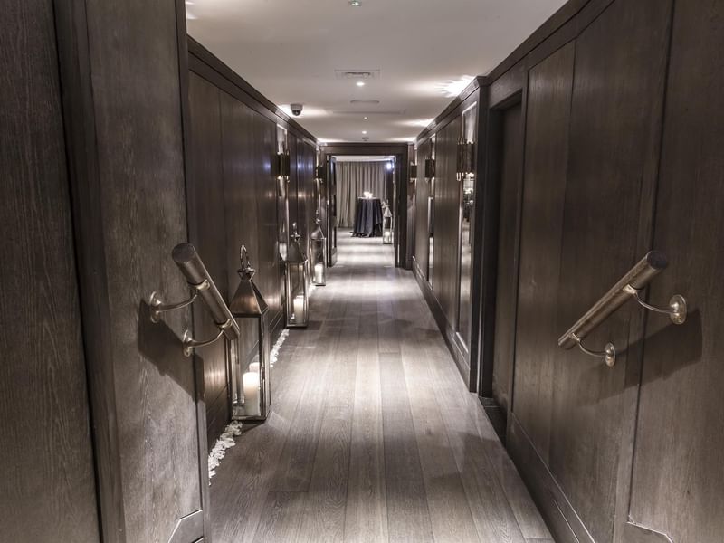 Elegant hallway with dark wood paneling, lighted sconces, and a long wooden floor at The May Fair Hotel leading up to the Private Dining Room.