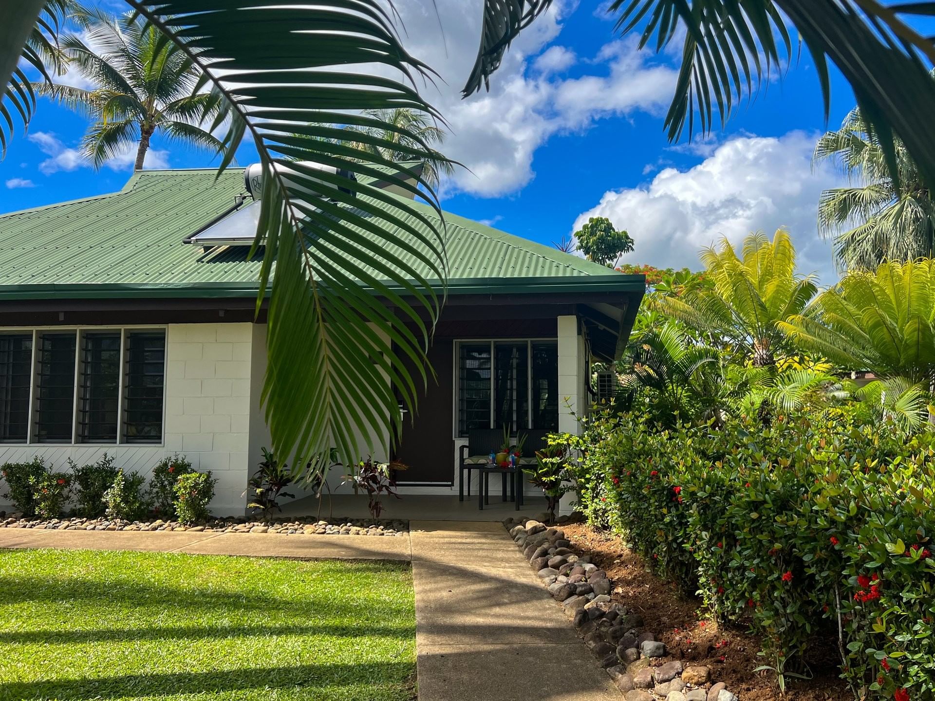 White-walled tropical villa with a green roof and a private veranda nestled among lush palms at TokaToka Resort Nadi Fiji