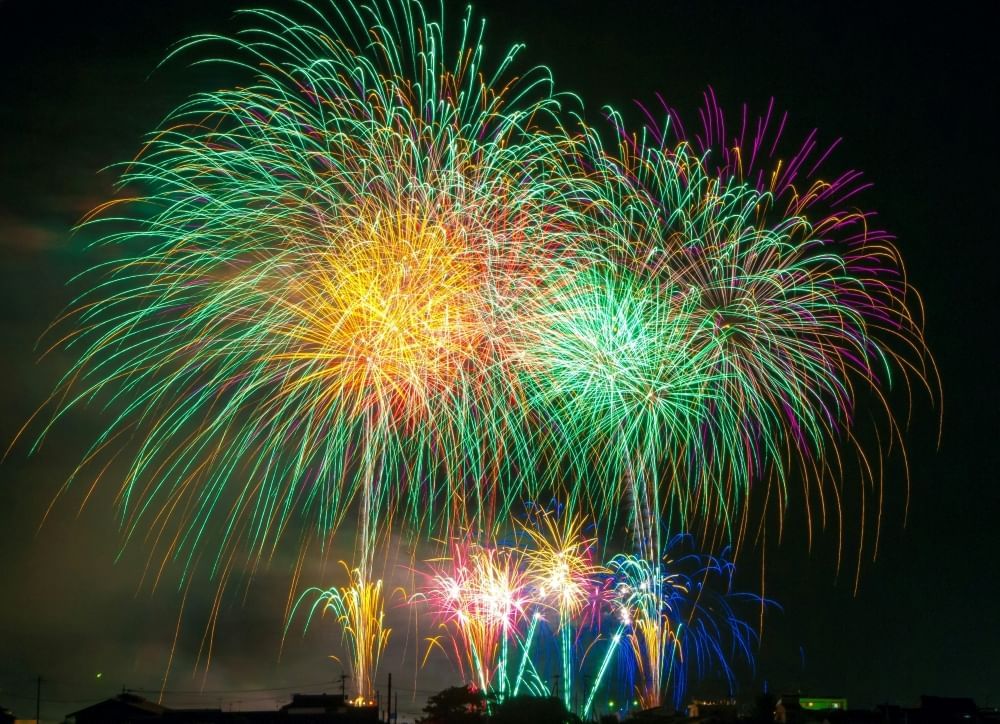 Green, yellow, purple, and blue fireworks erupt against a night sky.