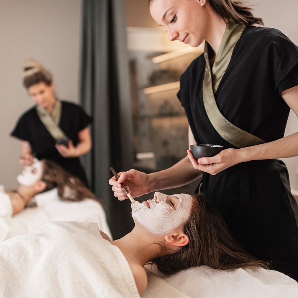 Estetista applica maschera viso a cliente durante un trattamento di bellezza.