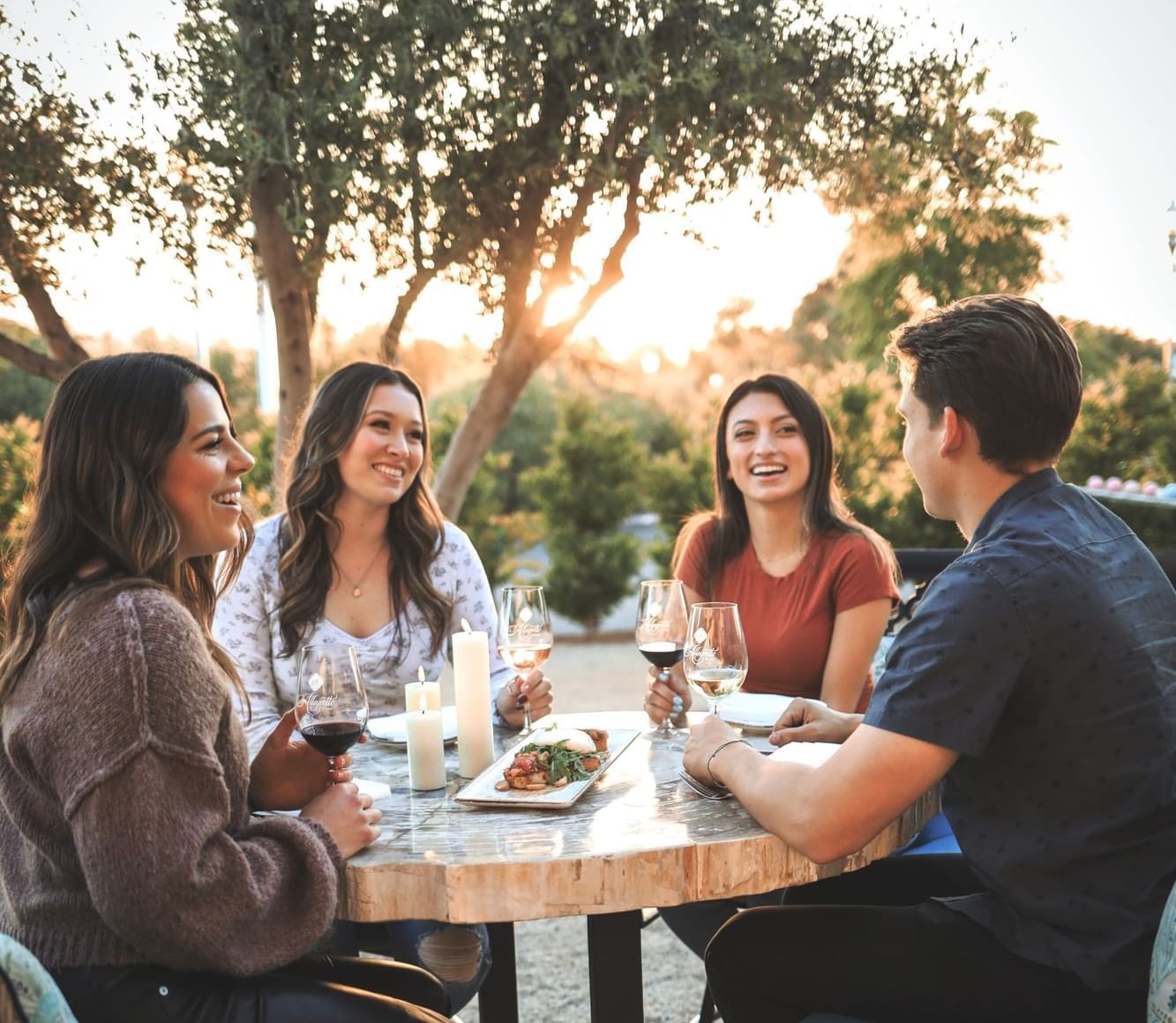 Four people sitting around an outdoor table smiling with wine and food