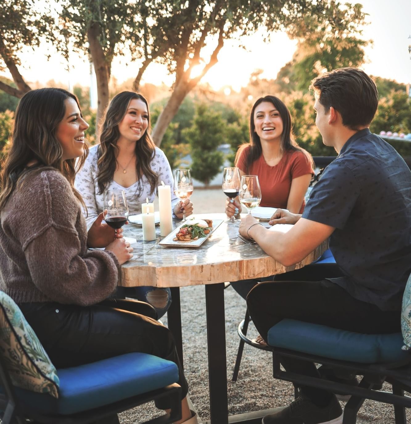 Four people sitting around an outdoor table smiling with wine and food