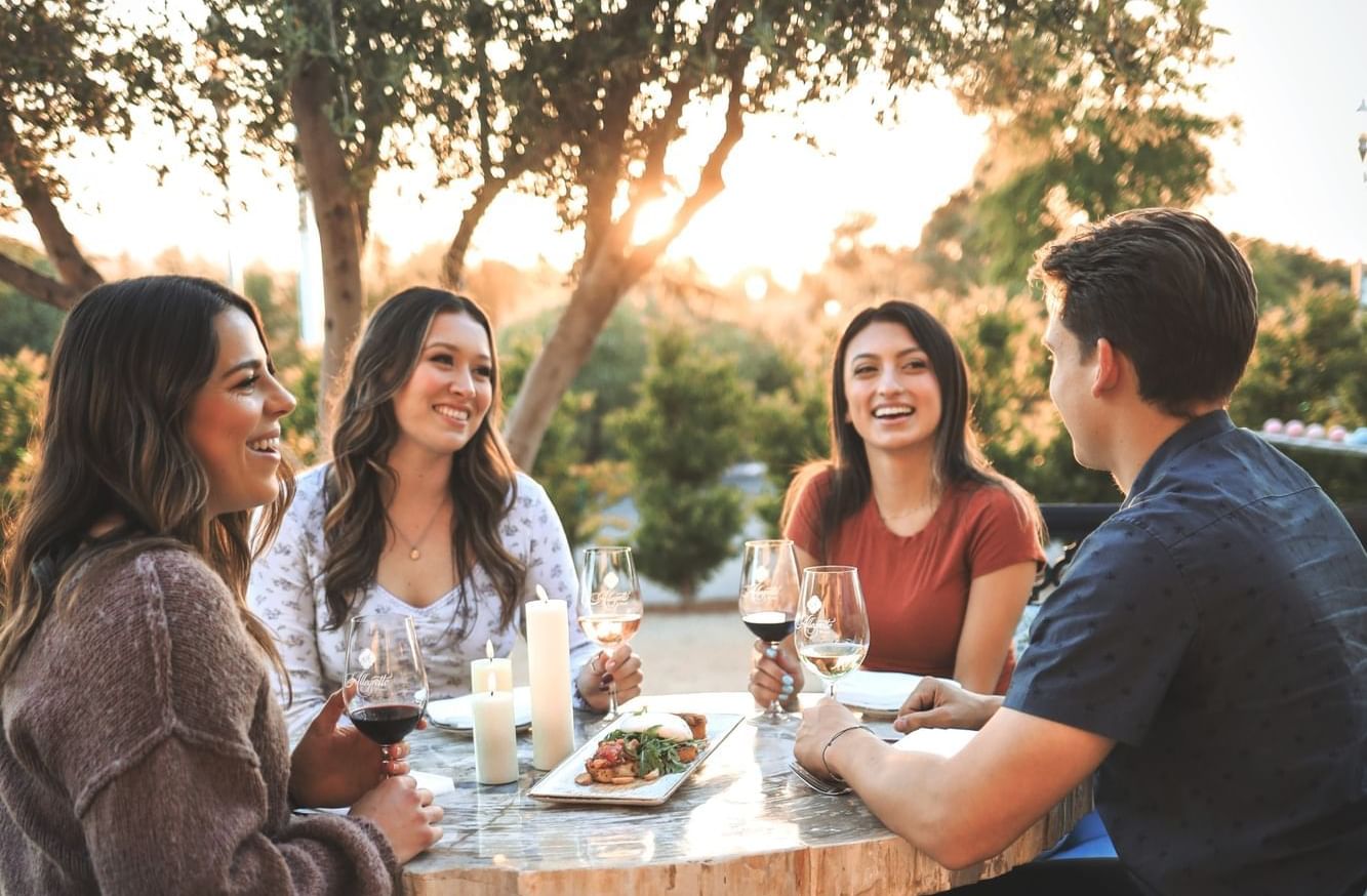 Four people sitting around an outdoor table smiling with wine and food