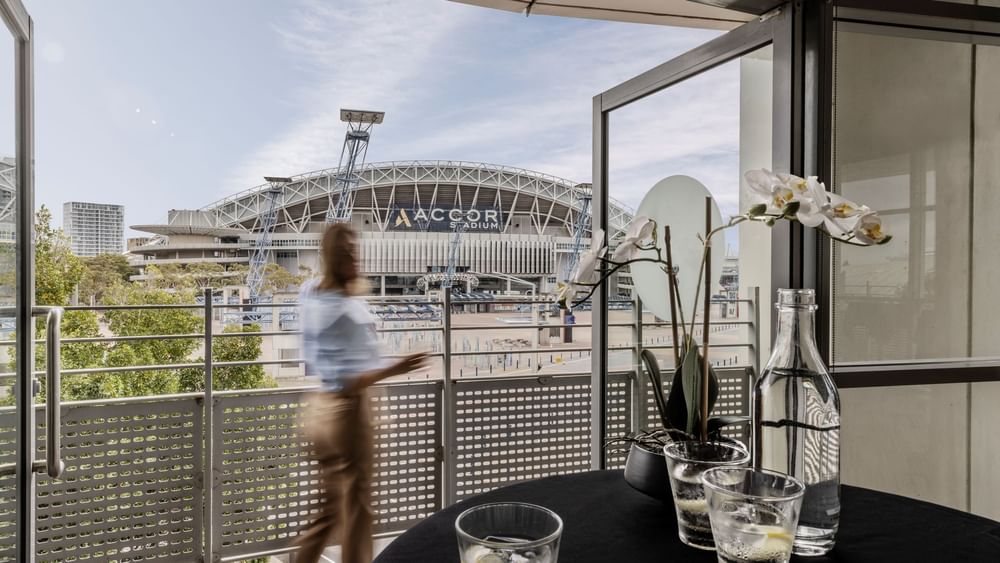 Blurred figure walking past a balcony table overlooking Accor Stadium in Marine Room at Novotel Sydney Olympic Park