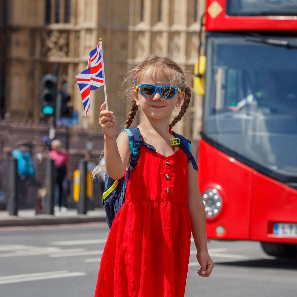 Child in a red dress holding a flag by a red bus on a city street near The Capital Hotel, Apartments and Townhouse