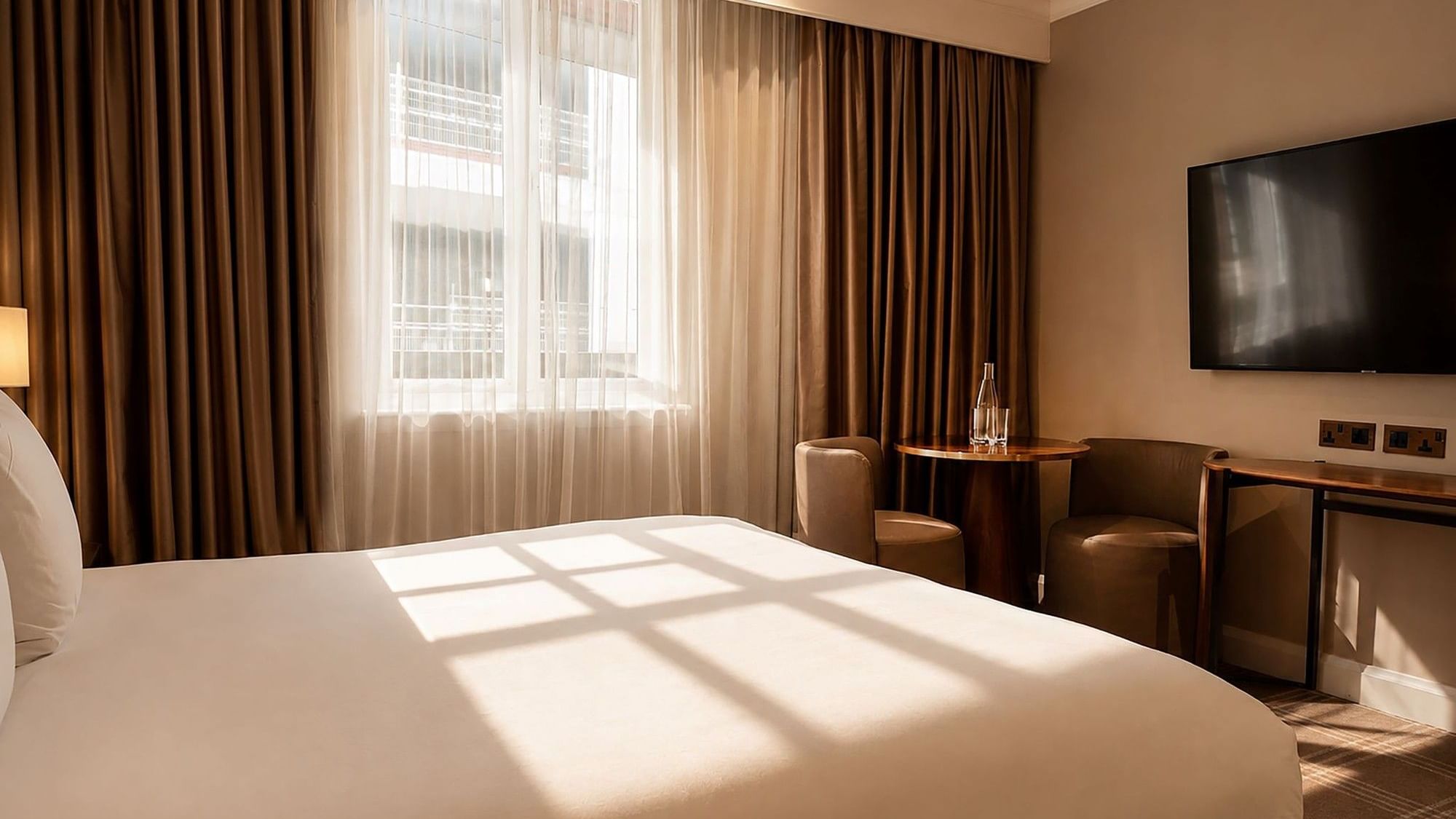 Sunlit Collection Superior Room with white bed, brown curtains, desk, and armchairs at The May Fair Hotel, London.