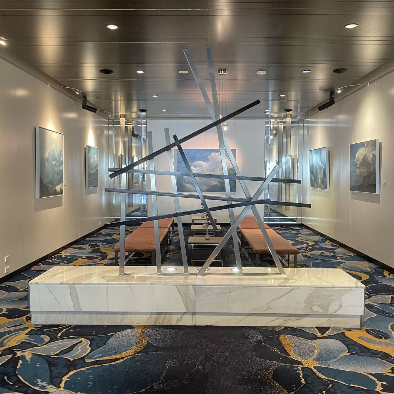 A large art piece displayed in a hallway with benches for seating Sofitel Brisbane Central