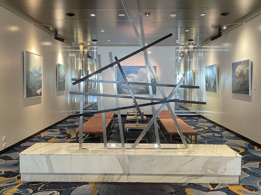 A large art piece displayed in a hallway with benches for seating Sofitel Brisbane Central