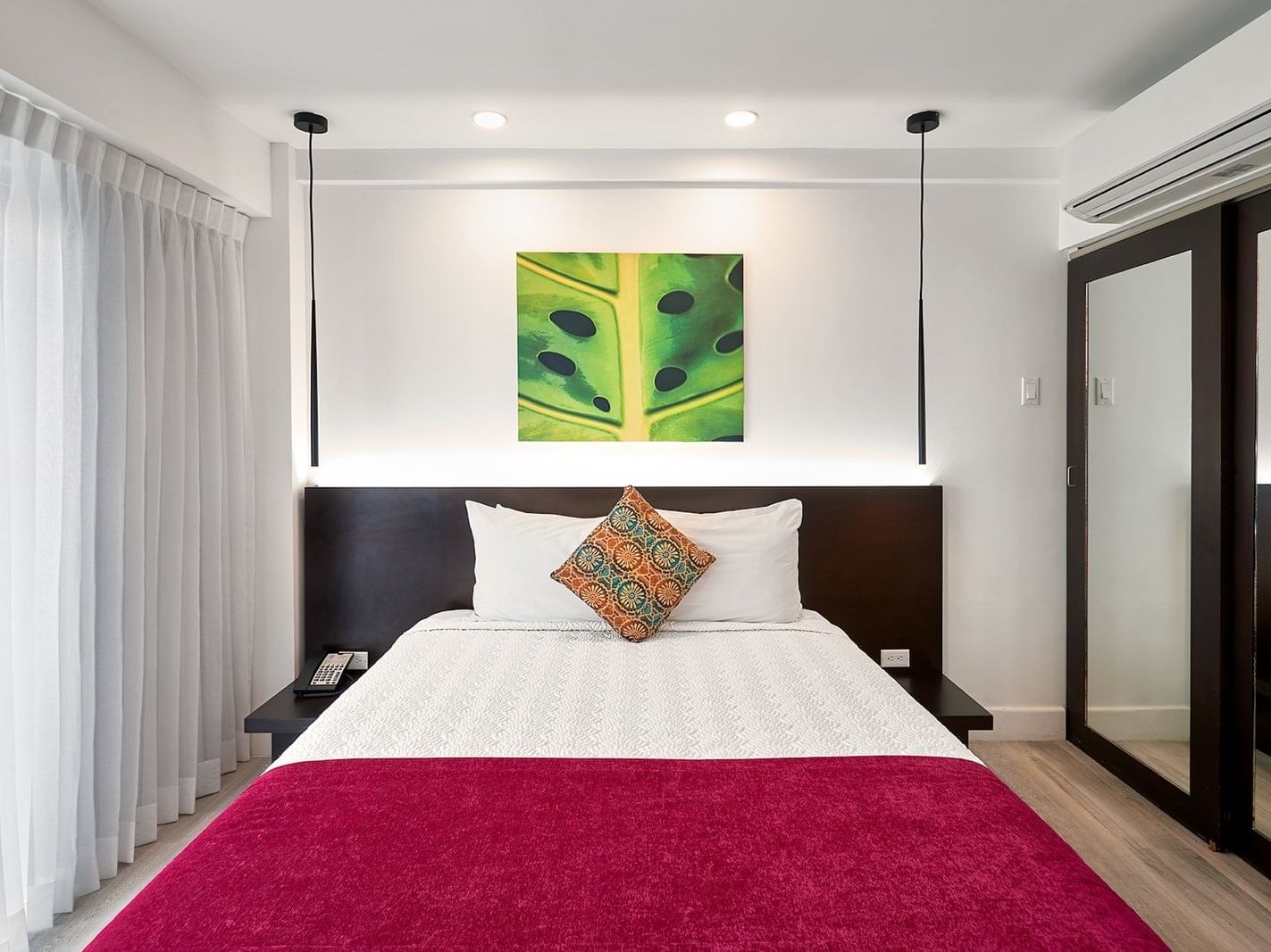 Queen bed with white linens, vibrant red runner, and green leaf artwork in Queen Room With Balcony at R Hotel Kingston