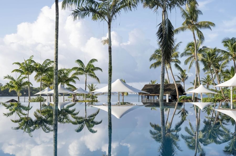 Palm trees and white umbrellas perfectly reflected in the still surface of an infinity pool at Warwick Le Lagon - Vanuatu