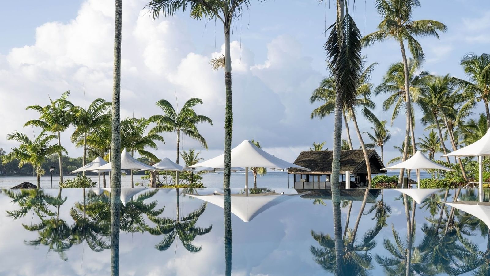 Palm trees and white umbrellas perfectly reflected in the still surface of an infinity pool at Warwick Le Lagon - Vanuatu