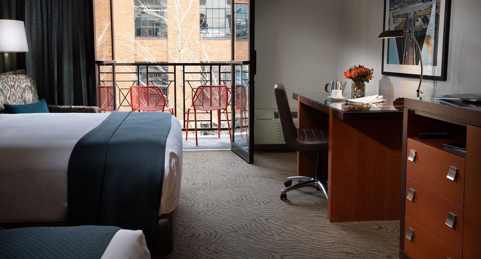A hotel room with a queen bed, desk, and balcony