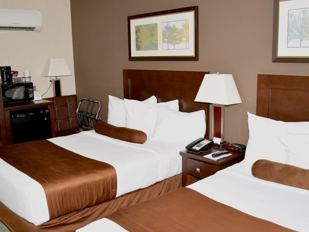 Hotel room with two beds, nightstand with lamp, mini fridge, microwave, and framed art on the walls.