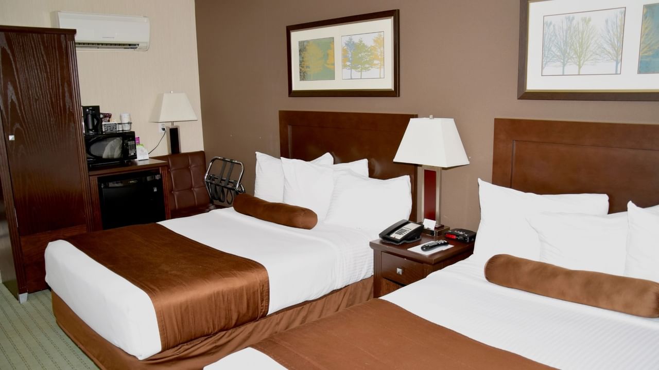 Hotel room with two beds, nightstand with lamp, mini fridge, microwave, and framed art on the walls.