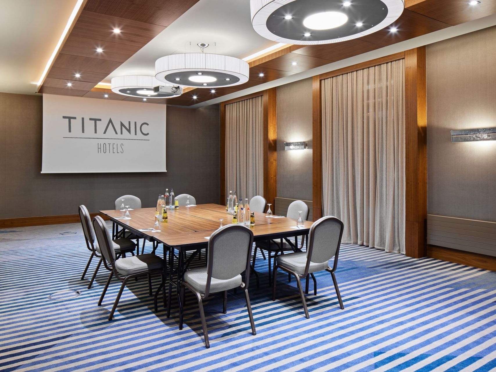 Konferenzraum mit langem Tisch, Stühlen, Vorhang und Wandbeschilderung – Titanic Chaussee Berlin.