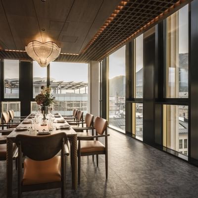 Sala da pranzo con tavoli e sedie, grandi finestre, vista sulla città e montagne.