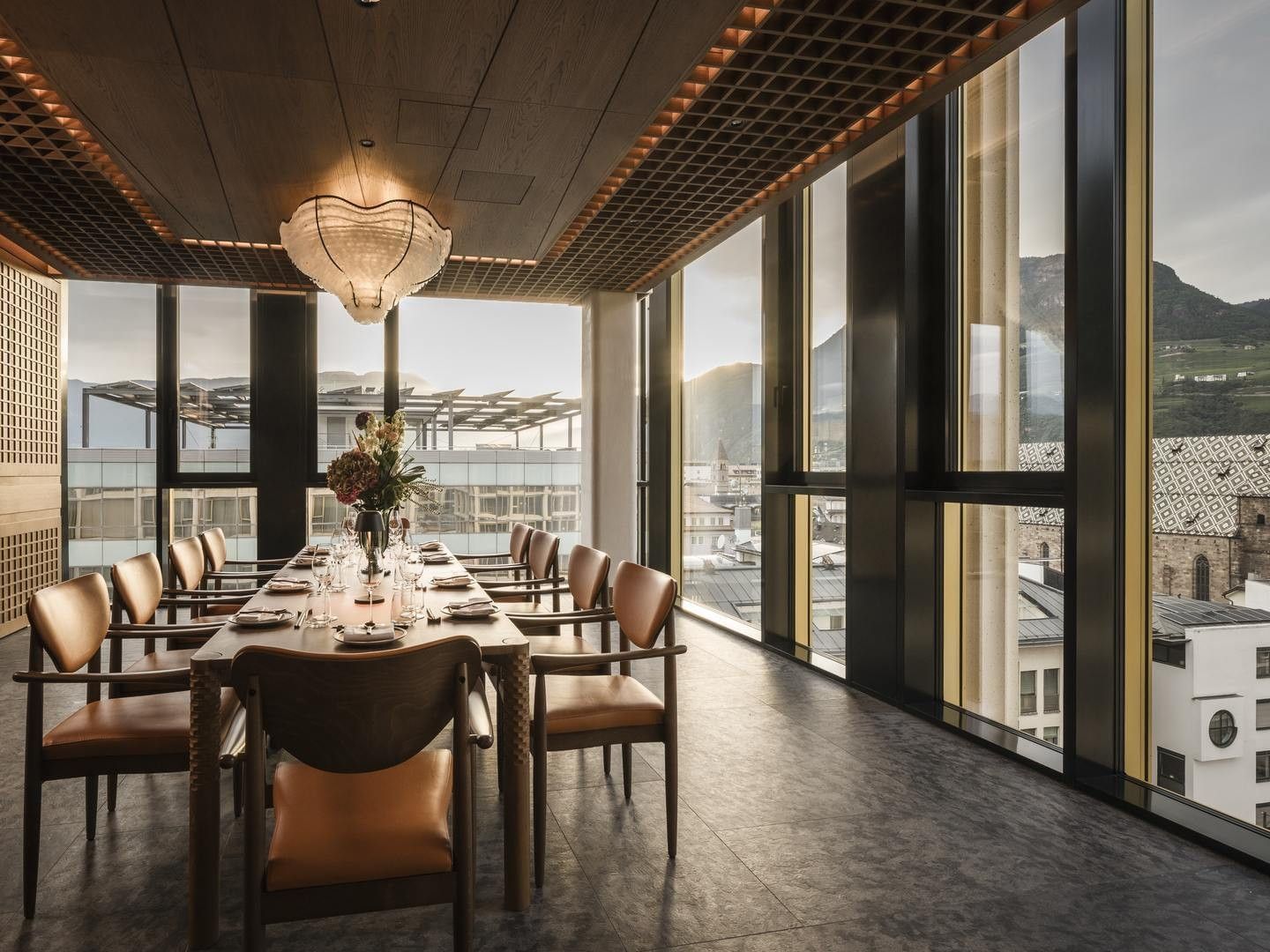 Sala da pranzo con tavoli e sedie, grandi finestre, vista sulla città e montagne.