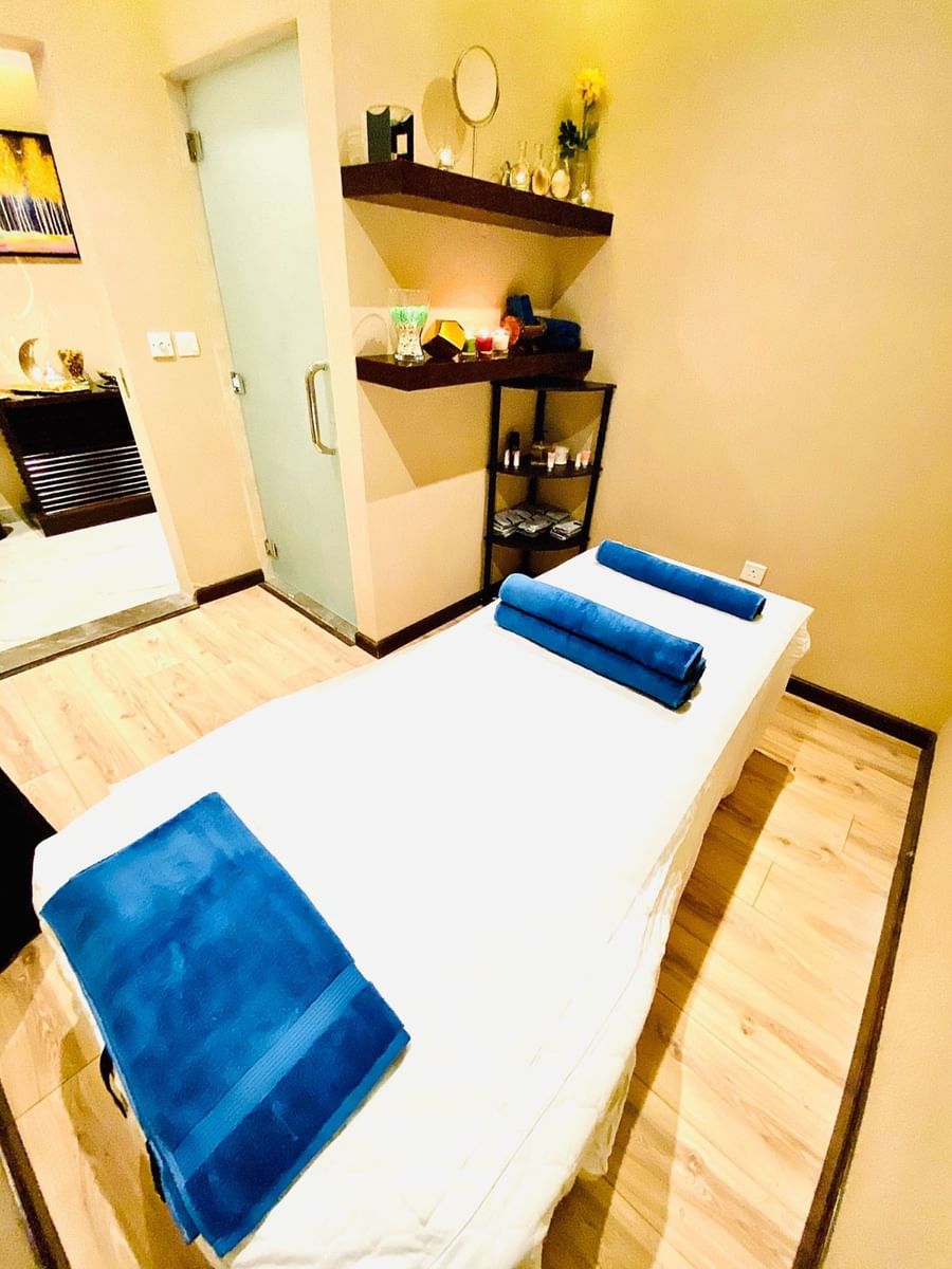 Massage bed with blue rolled towels by a glass door in Gold Spa at Naviti By Warwick Dammam