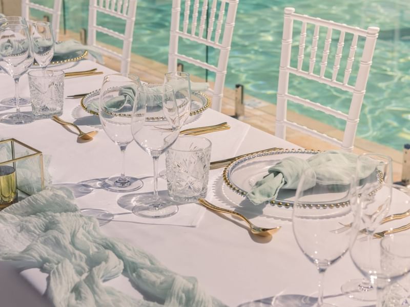 Outdoor table setting with white chairs by a pool at Pullman Port Douglas