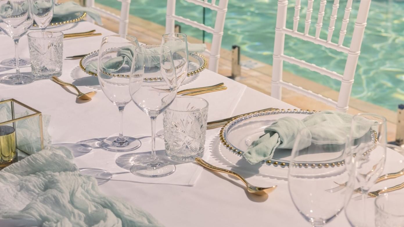 Outdoor table setting with white chairs by a pool at Pullman Port Douglas