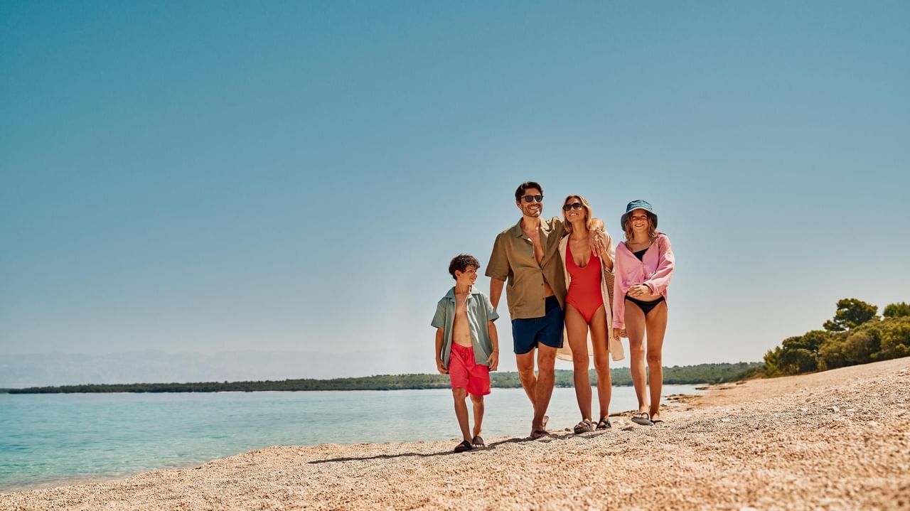 Famiglia di quattro persone in abbigliamento da spiaggia che cammina lungo la spiaggia.