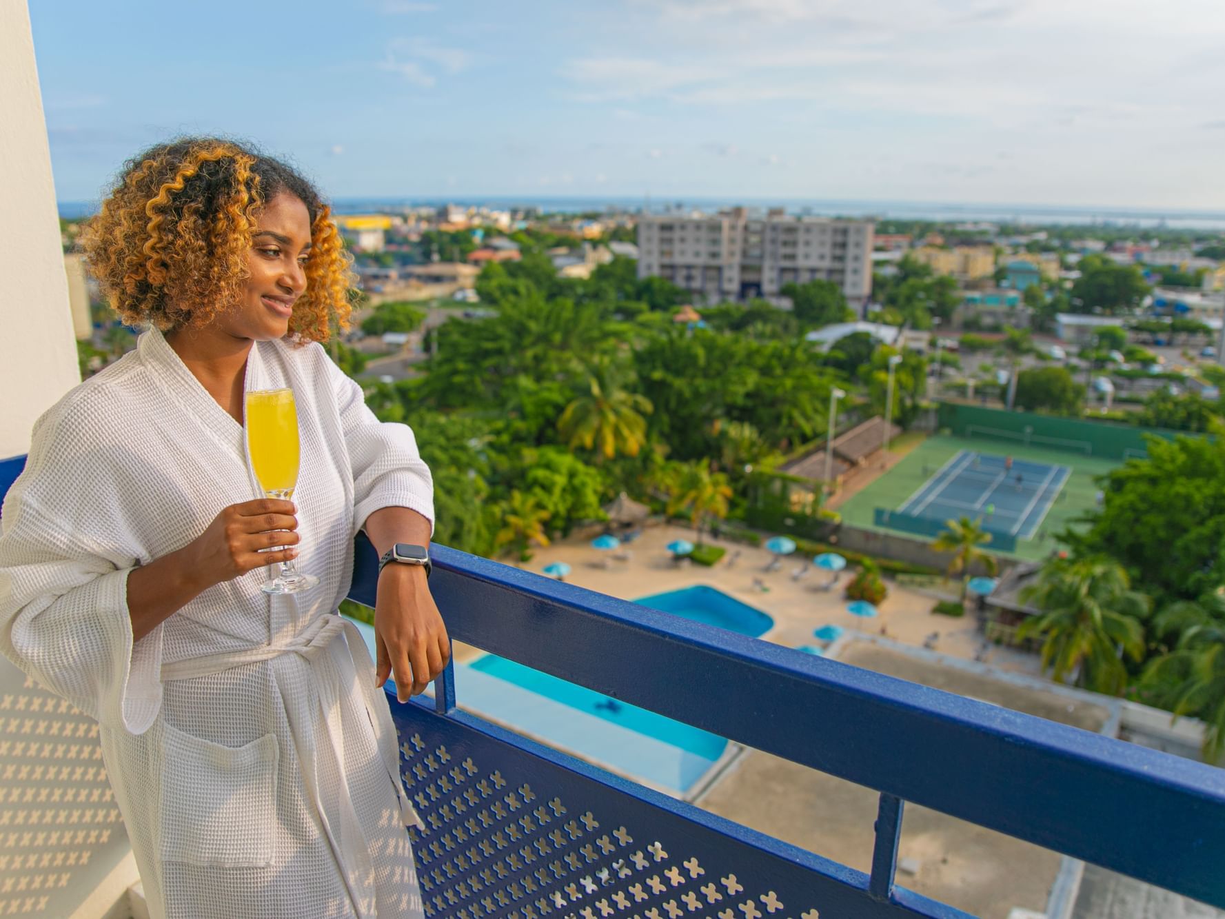 A lady enjoying fresh juice from balcony in Deluxe Room at Jamaica Pegasus Hotel