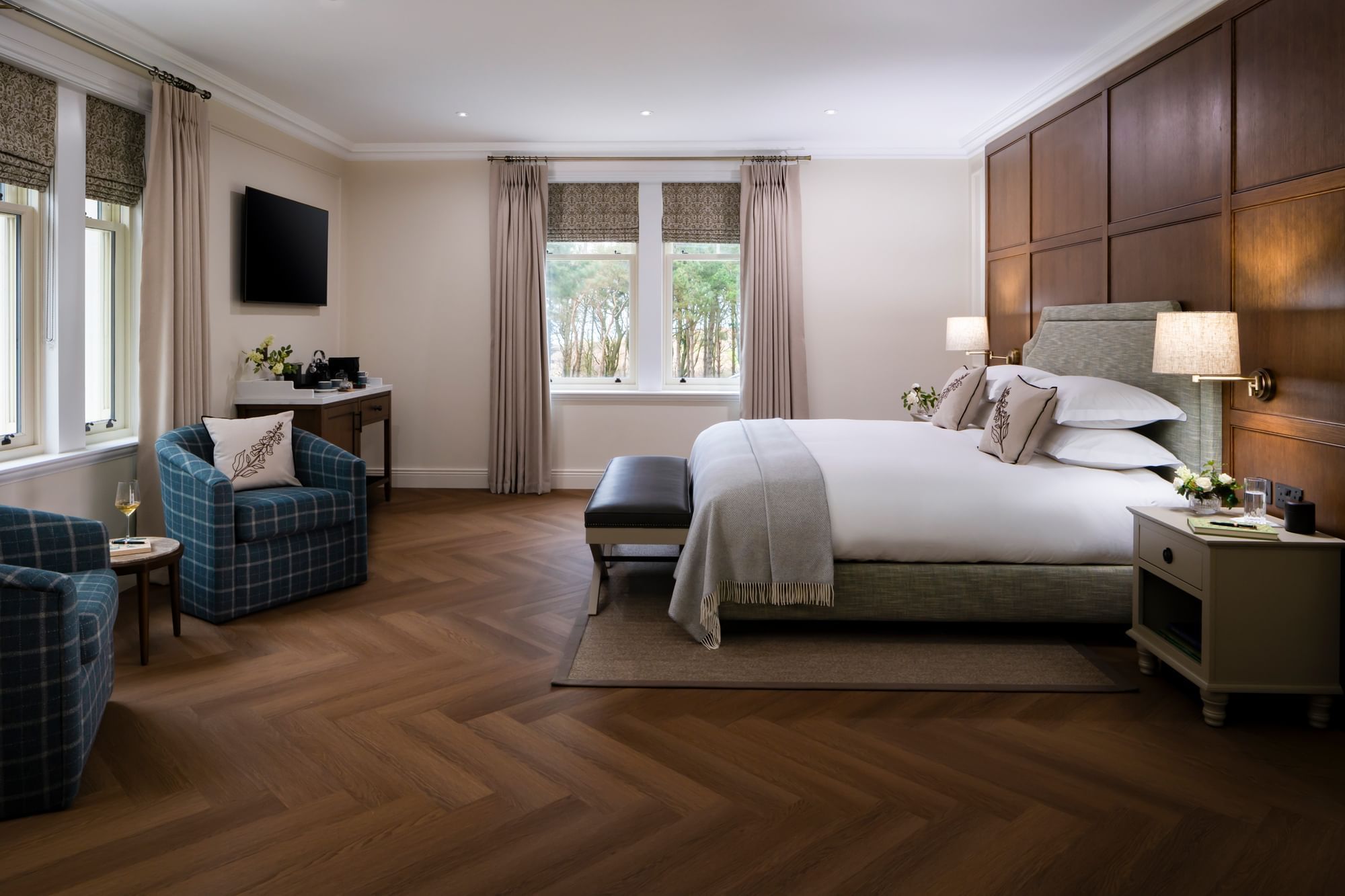 A stunning guest suite at Dunluce Lodge with a king-size bed, two armchairs, and a TV mounted on the wall